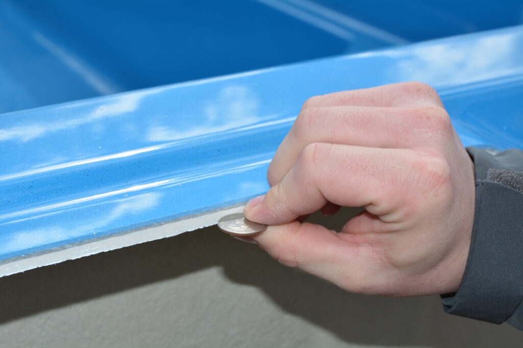 showing our fiberglass pool thickness by holding a quarter next to it